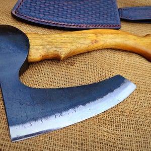 Puede incluir: Un hacha de mano negra y plateada con mango de madera. El hacha está sobre una superficie de arpillera marrón.