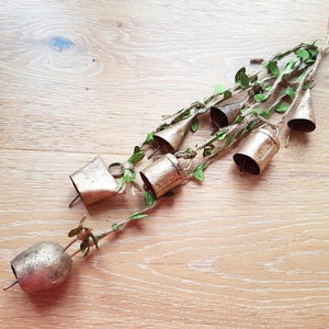 Peut inclure: Un carillon en métal doré avec plusieurs cloches suspendues à une ficelle avec des feuilles vertes. Les cloches sont disposées en cascade.