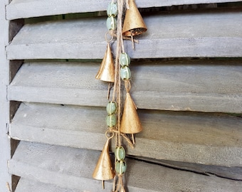May include: A string of gold bells with green beads hanging from a wooden shutter. The bells are arranged in a cascading pattern, with the largest bell at the top and the smallest bell at the bottom.