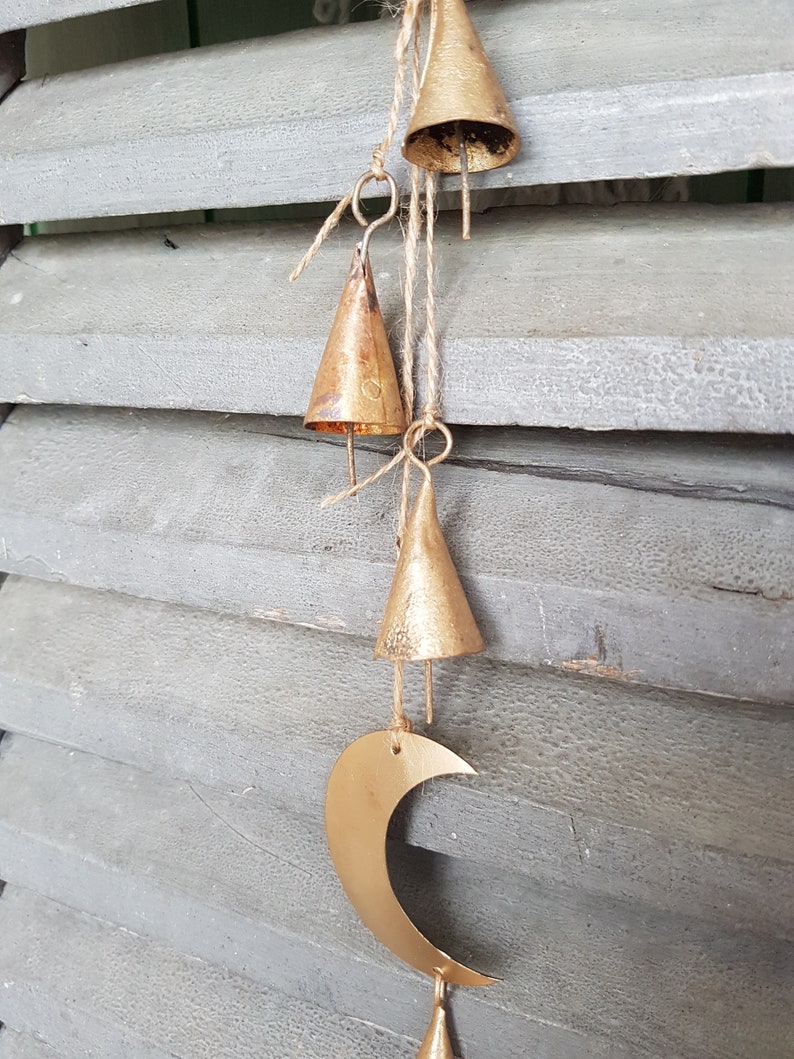May include: A gold-colored wind chime with a crescent moon shape and multiple small bells hanging from it. The chime is hanging from a wooden surface.