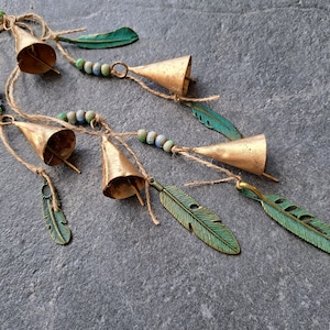 May include: A string of gold bells with green feathers and beads hanging from a twine cord.