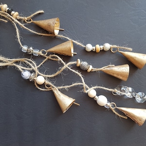 Peut inclure: Un carillon doré avec plusieurs cloches, des perles et un prisme de cristal suspendu à une ficelle. Les cloches sont de différentes tailles et formes, et les perles sont blanches, argentées et noires.