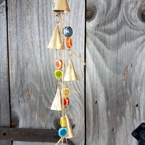 Op de afbeelding: Een gouden windgong met kleine bellen en kleurrijke kralen die aan een houten deur hangen.