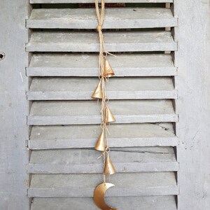 May include: A gold metal crescent moon with a string of small gold bells hanging from it. The bells are attached to a natural twine string.