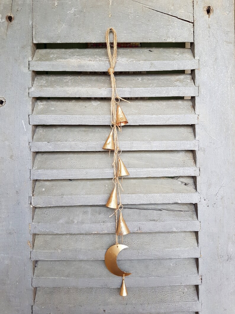 May include: A gold metal crescent moon with a string of small gold bells hanging from it. The bells are attached to a natural twine string.