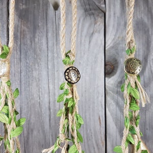 Op de afbeelding: Drie macram&eacute; plantenhangers met verschillende gekleurde kralen en groene bladeren die aan een houten muur hangen.