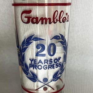 May include: A clear glass tumbler with a red and blue design. The glass has the words "Gamble's 20 Years of Progress" printed on it.