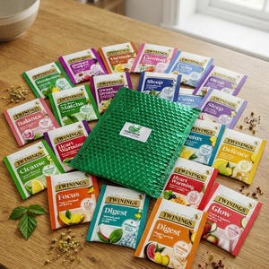 Może przedstawiać: Kolekcja różnych torebek herbaty Twinings w kolorowych papierowych saszetkach, ułożonych wokół zielonej koperty bąbelkowej. Torebki z herbatą posiadają etykiety takie jak Balance, Matcha, Cleanse, Focus, Heart Warming, Digest, Glow, Defence, Detox, Sleep, Calm, Unwind, Turmeric oraz Sweet Dreams.