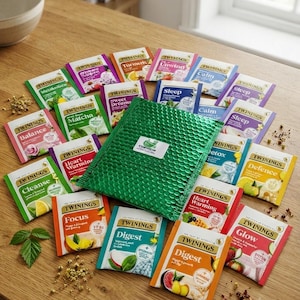 Könnte beinhalten: Eine Sammlung verschiedener Twinings-Teebeutel in bunten Einzelverpackungen, angeordnet um einen grünen Luftpolsterumschlag mit weißem Etikett. Die Teesorten umfassen Balance, Matcha, Cleanse, Focus, Digest, Heart Warming, Glow, Defence, Detox, Sleep, Calm, Unwind, Turmeric und Sweet Dreams.