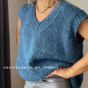 Puede incluir: Un chaleco de punto azul sin mangas con cuello en V. El chaleco tiene un punto ligeramente texturizado y se lleva sobre unos vaqueros plateados. El texto "VESTFAVORITE_BY_TRENDS" es visible en la parte inferior de la imagen.