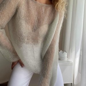 Può includere: Un maglione di maglia leggera di colore verde chiaro, con una vestibilità ampia e maniche lunghe.