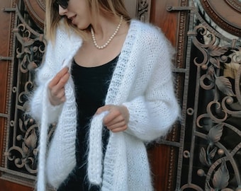 May include: A white fuzzy cardigan with long sleeves and a tie at the waist. The cardigan is made of a soft, fluffy yarn and has a relaxed fit.