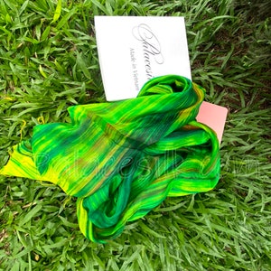 Może przedstawiać: Zielono-żółty jedwabny szal w paski. Szal jest złożony i leży na zielonej trawie. Na białym pudełku w tle widnieje napis "Palacesilk Made in Vietnam".