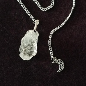 May include: A clear quartz crystal wrapped in wire, hanging from a silver chain with a crescent moon charm. The crystal is a natural, irregular shape.