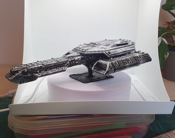 Può includere: Un modello di nave spaziale nero e argento, con dettagli intricati, è esposto su un giradischi bianco. Il modello è allestito in una scatola di fotografia bianca con uno sfondo bianco.