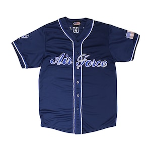 May include: A navy blue baseball jersey with white piping and a blue and white "Air Force" logo on the front. The jersey has a button-up front and a small American flag patch on the right sleeve.