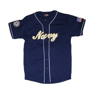 May include: A navy blue baseball jersey with white piping and buttons. The jersey has a large yellow "Navy" wordmark on the front and a small US Navy emblem on the left sleeve. The right sleeve has a small American flag patch.