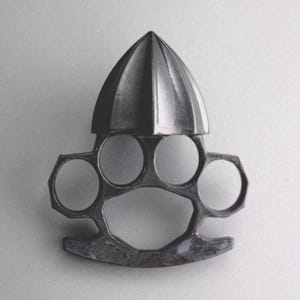 May include: A black metal citrus juicer with a knuckle duster design. The juicer has a pointed top and four holes for fingers.