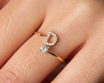 Può includere: Un anello d'oro con un solo diamante e la lettera "D" incastonata con diamanti più piccoli. L'anello è su un dito.