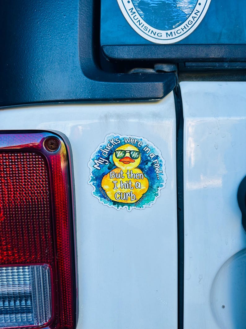May include: A yellow rubber duck with sunglasses is on a sticker that says "My ducks were in a row... But then I hit a curb."