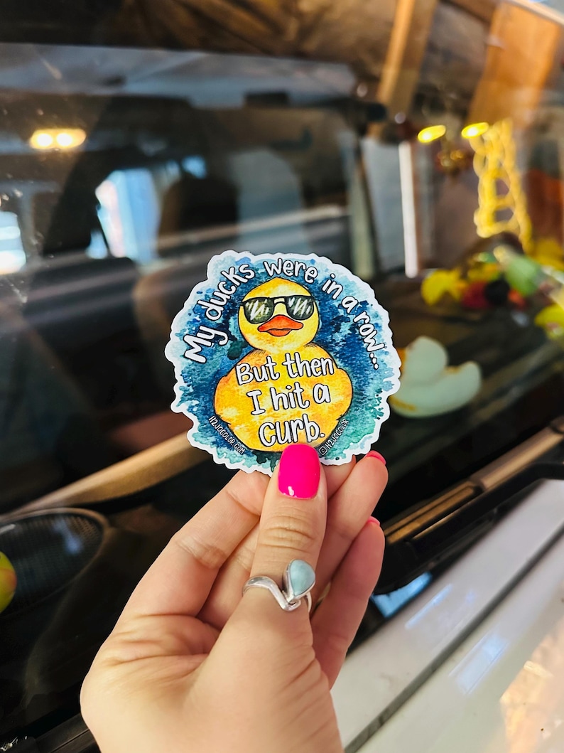 May include: A yellow rubber duck with sunglasses and a blue watercolor background. The duck has text that reads "My ducks were in a row... But then I hit a curb."