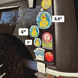 May include: A black Jeep with a variety of stickers on the back window. The stickers are different sizes and feature a variety of designs, including a duck, a jackalope, a turtle, and a mountain range. The stickers are 3 inches, 4 inches, and 5.5 inches in size.