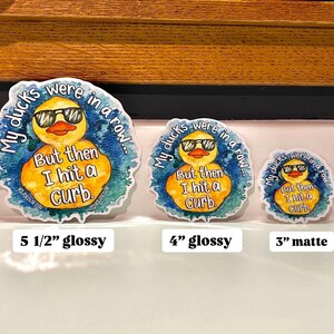 May include: Three yellow rubber duck stickers with a watercolor background. The ducks are wearing sunglasses and the text reads "My ducks were in a row... But then I hit a curb." The stickers are available in three sizes: 5 1/2 inches, 4 inches, and 3 inches. The 5 1/2 inch and 4 inch stickers are glossy, while the 3 inch sticker is matte.