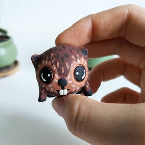 May include: A small, brown and black hand-painted clay figurine of a cartoon animal with large eyes and a toothy grin.