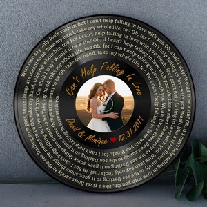 May include: A black vinyl record featuring a central photograph of a couple, encircled by song lyrics. The record displays the text "Can't Help Falling in Love," names, and a date.