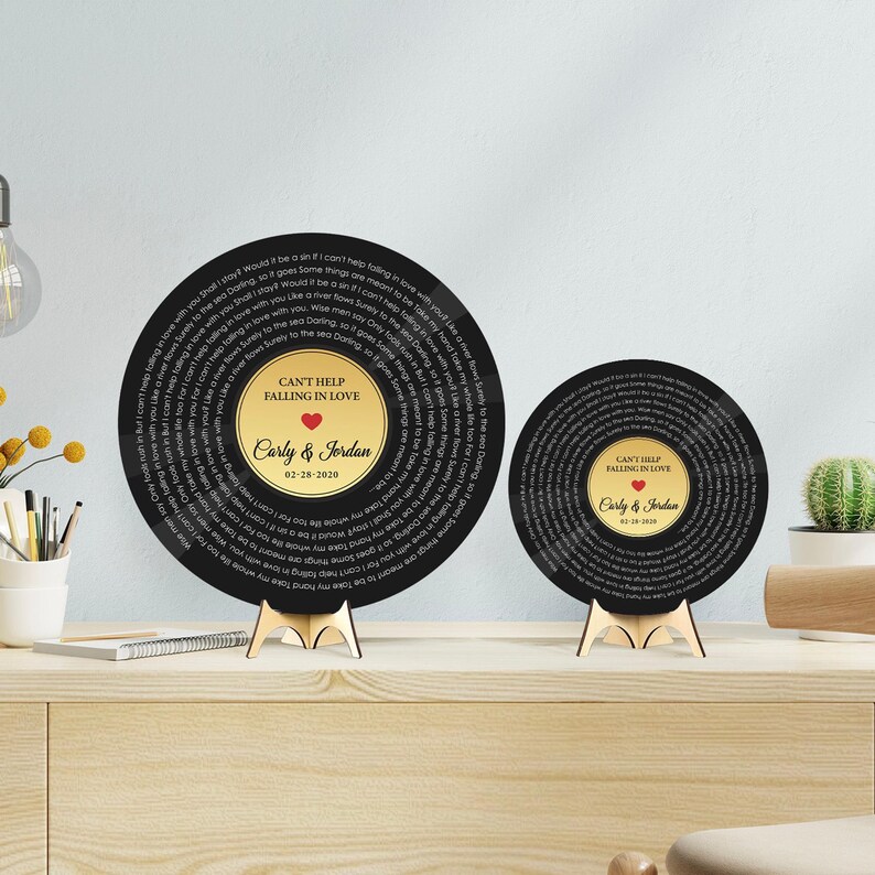 May include: Two circular black plaques designed like vinyl records, featuring lyrics to Can't Help Falling in Love, a central gold label with the text Can't Help Falling in Love, Carly & Jordan, and a date, all supported by small wooden stands.