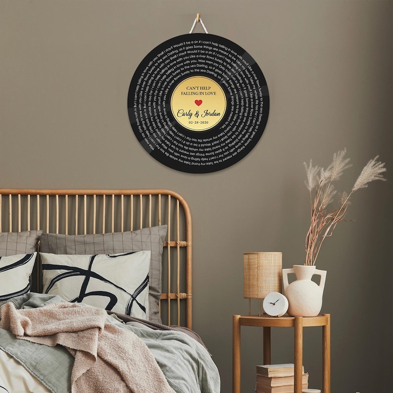 May include: A circular wall hanging resembling a vinyl record with black outer edges featuring lyrics to Can't Help Falling in Love. The center gold label displays the text Can't Help Falling in Love, a red heart, Carly & Jordan, and 02-28-2020.
