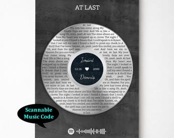 May include: A rectangular wall art print featuring the song title AT LAST in black text at the top. A circular vinyl record graphic displays the song lyrics in a spiral pattern. The center label shows the names Imani and Dennis with the date 12.16.2000 and a heart icon. A scannable music code is at the bottom.