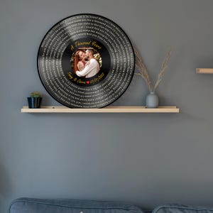 May include: A circular wall plaque designed like a vinyl record featuring a central photograph of a couple. The text A Thousand Years, Timmy & Cierra, and 07/01/2022 is printed on the record, surrounded by lyrics in a circular pattern.
