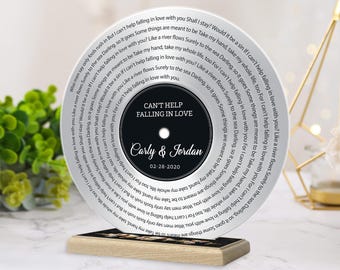 May include: A circular acrylic plaque designed like a vinyl record, featuring the song title Can't Help Falling in Love, the names Carly & Jordan, the date 02-28-2020, and lyrics spiraling around the center on a light gray background.