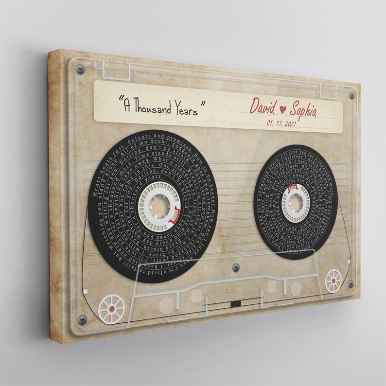 May include: A canvas print featuring a vintage cassette tape design. The tape includes the text "A Thousand Years", names "David & Sophia", and the date 01.11.2021. The tape reels are black with white text, and the background is beige.