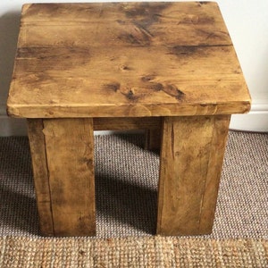 May include: A rustic wooden side table with a natural wood finish. The table has a square top and four legs. The table is sitting on a woven rug.