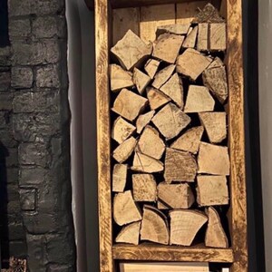 May include: A rustic wooden log rack with two shelves, one for larger logs and one for smaller kindling. The rack is stained a dark brown and has black hairpin legs. It is filled with stacked logs and kindling.