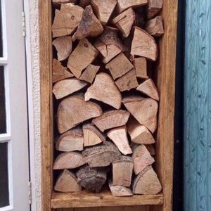 May include: A wooden log rack with two shelves. The top shelf is filled with stacked logs of wood. The bottom shelf is filled with smaller pieces of kindling. The rack is standing on four black metal hairpin legs.