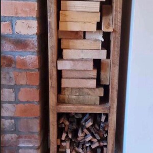 May include: A rustic wooden log storage rack with two shelves. The top shelf is filled with stacked wooden planks, and the bottom shelf is filled with kindling. The rack is standing on four black metal legs.