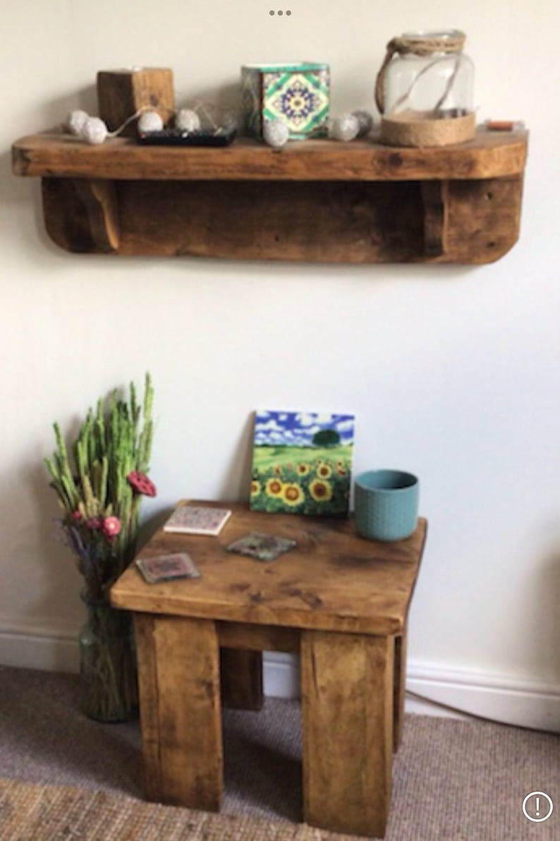 May include: A rustic wooden shelf with a decorative tile box and string lights. Below the shelf is a small wooden table with a sunflower tile, coasters, and a teal blue cup.
