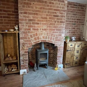 May include: A wood-burning fireplace with a black cast iron stove in a brick fireplace. The fireplace is in a living room with a wooden cabinet and a couch.
