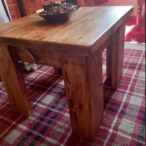 May include: A rustic wooden coffee table with a thick, natural wood top and sturdy legs. The table is sitting on a red and white plaid rug.
