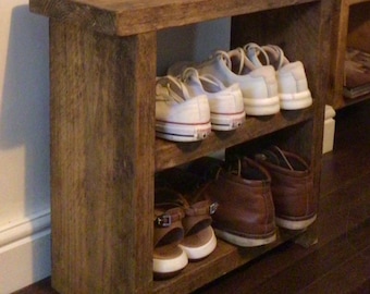 May include: A rustic wooden shoe rack with two shelves. The top shelf is a bench and the bottom shelf is for shoes. There are white sneakers and brown boots on the shelves.