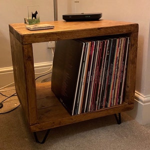 May include: A rustic wooden record player stand with a black vinyl record collection and hairpin legs. The stand has a natural wood finish and is perfect for displaying your favourite records.