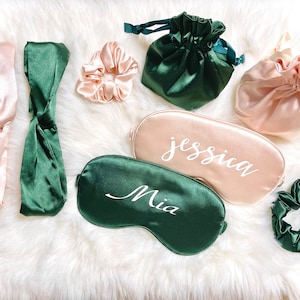 May include: An assortment of satin sleep accessories in shades of pink and emerald green. Items include headbands, scrunchies, drawstring bags, and personalized sleep masks with names like "Jessica" and "Mia" in white script.