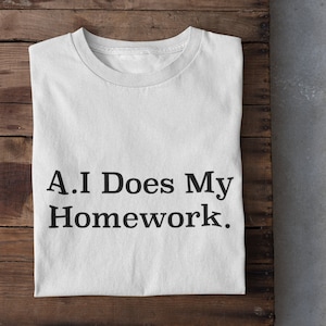 May include: White t-shirt with the text "A.I Does My Homework." printed on it. The shirt is folded and laid on a wooden surface.