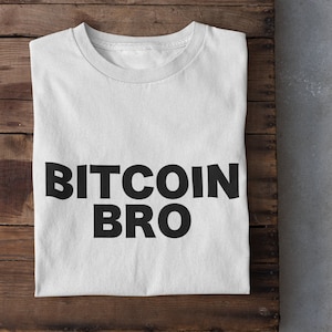 Puede incluir: Camiseta blanca con el texto "BITCOIN BRO" impreso en negro.