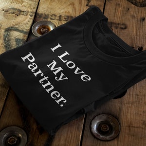 Może przedstawiać: Czarny T-shirt z białym napisem "Kocham mojego partnera."