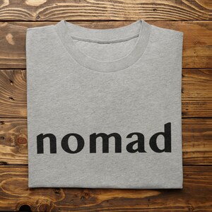 May include: A gray t-shirt with the word "nomad" printed in black on the front.