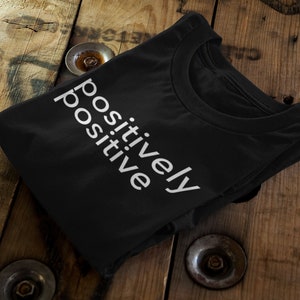 Puede incluir: Una camiseta negra con el texto "positively positive" impreso en blanco en la parte delantera.